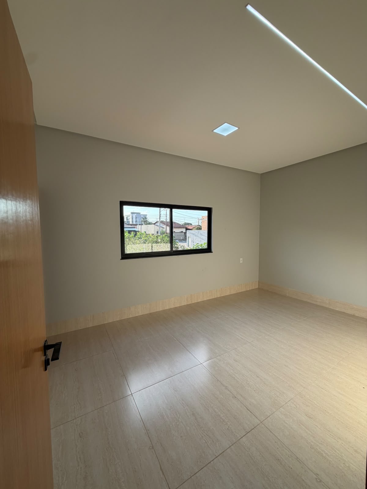 Quarto da suíte casal vazio, com janela de esquadria preta e rodapé alto
